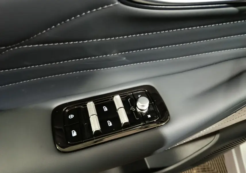 Gros plan sur les commandes de réglage des vitres et rétroviseurs sur la porte côté conducteur d’un Geely Starray gris clair.