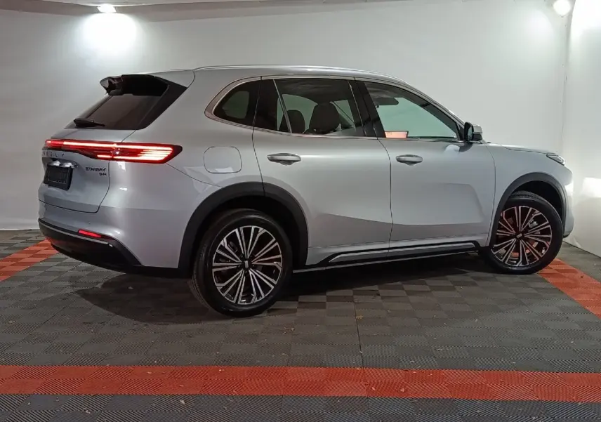 Vue de profil côté droit du SUV GEELY STARRAY gris clair avec feux arrière allumés dans un studio lumineux.