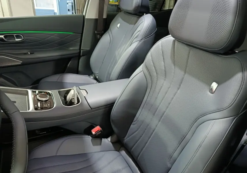 Vue intérieure rapprochée des sièges avant gris foncé en cuir perforé du GEELY STARRAY 1.5 EM-I PHEV Max+ avec accoudoir central.