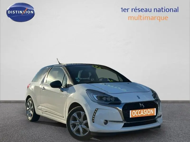 Vue 3/4 avant d'une DS3 blanche avec calandre chromée et jantes alu, stationnée devant un mur clair.