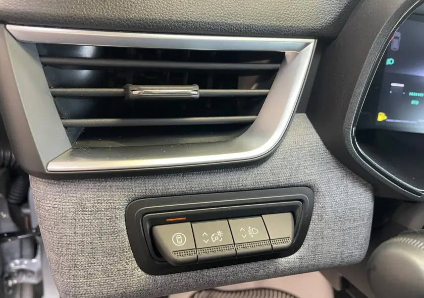 Détail de la console côté gauche avec aérateur chrome satiné et commandes d’éclairage sur tissu gris dans Renault Clio 2025.