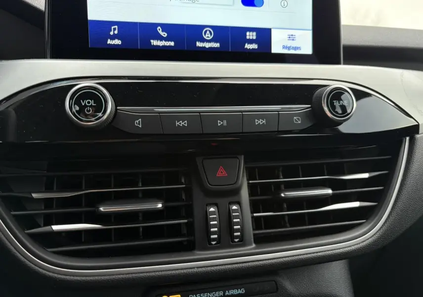 Gros plan sur la console centrale du Ford Kuga 2024, mettant en valeur l’écran tactile et les commandes audio noires brillantes.
