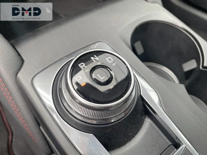 Gros plan sur la molette de sélection de la boîte automatique du Ford Kuga blanc Glacier, avec console et porte-gobelets visibles.