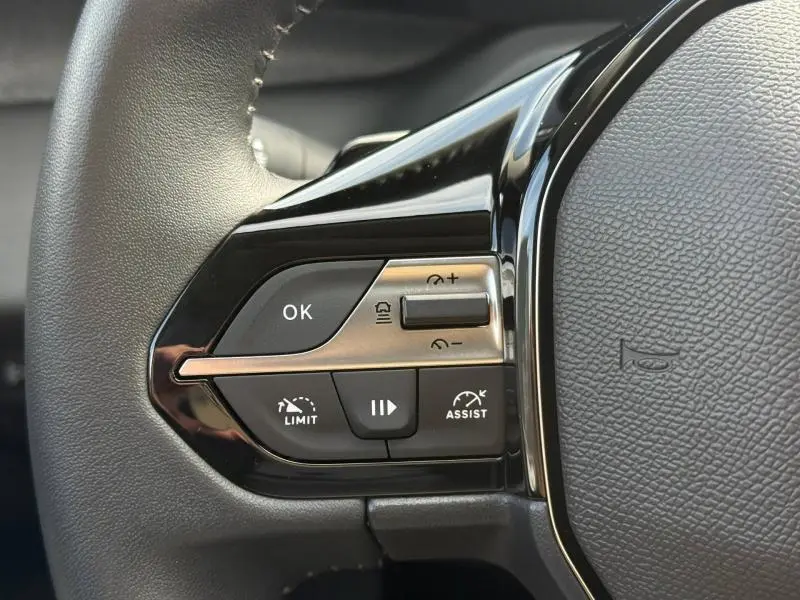 Gros plan sur les commandes gauche du volant noir du Peugeot 308 2024, avec boutons de régulateur et limiteur de vitesse.