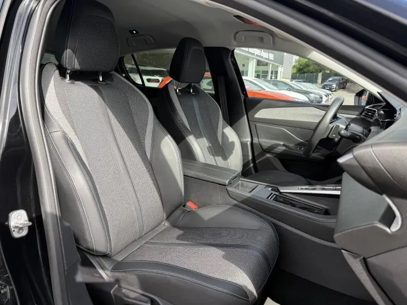 Vue intérieure côté gauche de la Peugeot 308 2024 Noir Perla Nera, sièges avant en tissu et cuir avec accoudoir central.