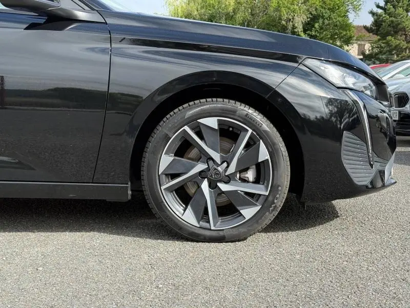 Vue de profil avant gauche sur la roue et partie avant d'une Peugeot 308 noire Perla Nera avec jante alu distinctive.