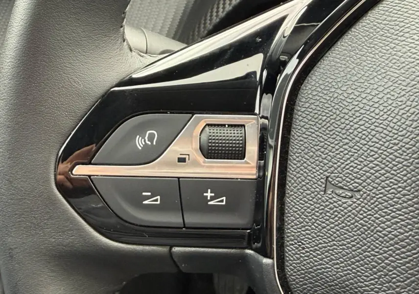 Gros plan sur les commandes audio au volant noir brillant de la Peugeot 208 1.2 100ch Allure 2025.
