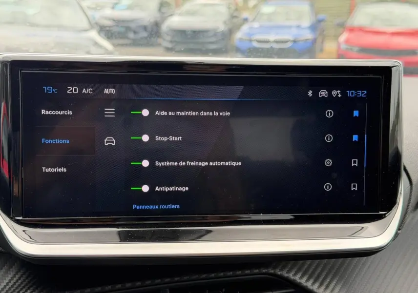 Écran tactile intérieur de la Peugeot 208 2025 affichant les aides à la conduite, avec reflet de voitures en arrière-plan.
