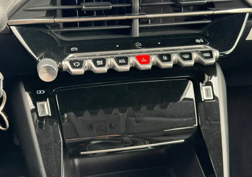 Vue rapprochée de la console centrale noire brillante du Peugeot 208 1.2 100ch Allure avec boutons chromés et touches fonctionnelles.
