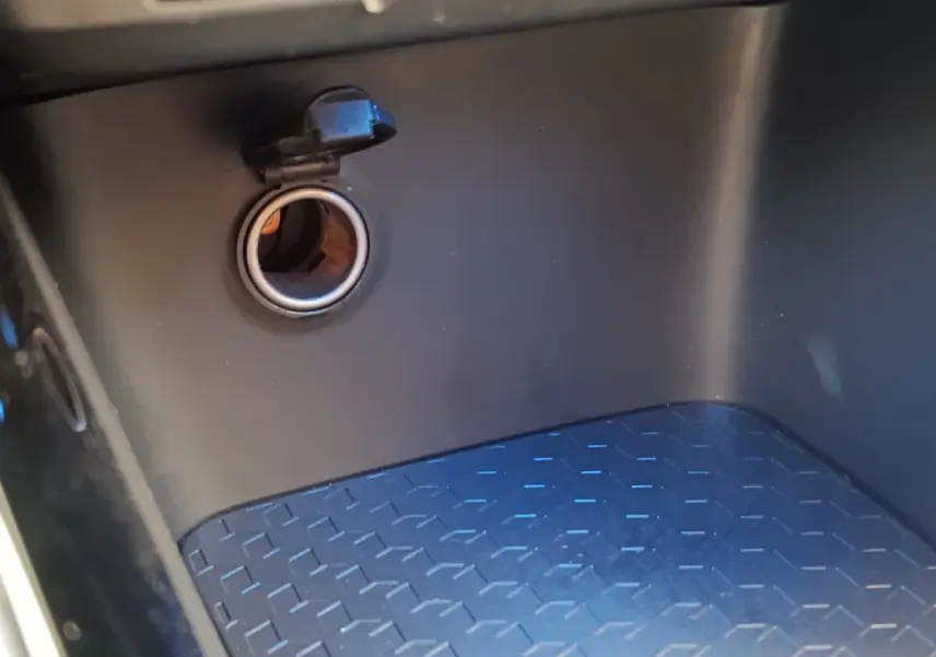 Prise 12V ouverte dans le compartiment de rangement intérieur noir de la Toyota Yaris Hybride 116h Collection 2022.