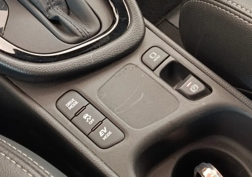 Gros plan sur la console centrale noire de la Toyota Yaris Hybride 116h avec boutons mode conduite et frein électrique.