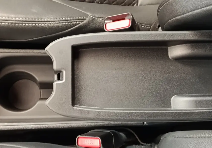 Vue rapprochée de la console centrale noire avec porte-gobelet et ceintures de sécurité rouges dans une Toyota Yaris blanche hybride.