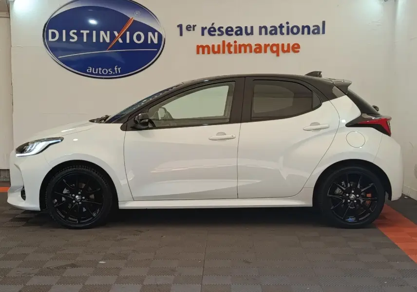Profil droit d'une Toyota Yaris Hybride 116h Collection blanche avec jantes noires et toit noir en intérieur showroom.