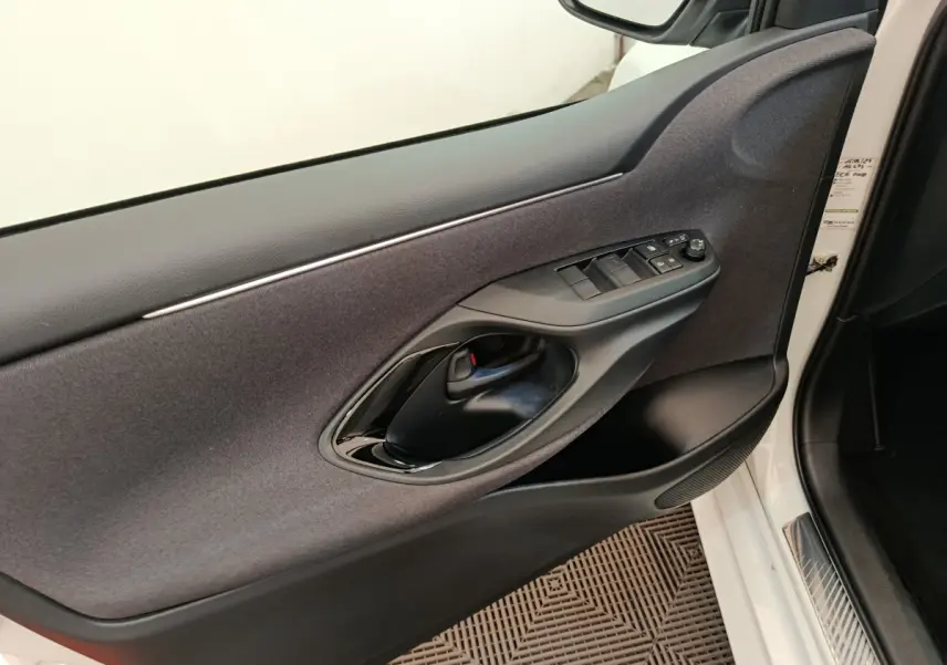 Vue intérieure côté conducteur de la porte d'une Toyota Yaris Hybride blanche, avec commandes électriques et poignée noire.