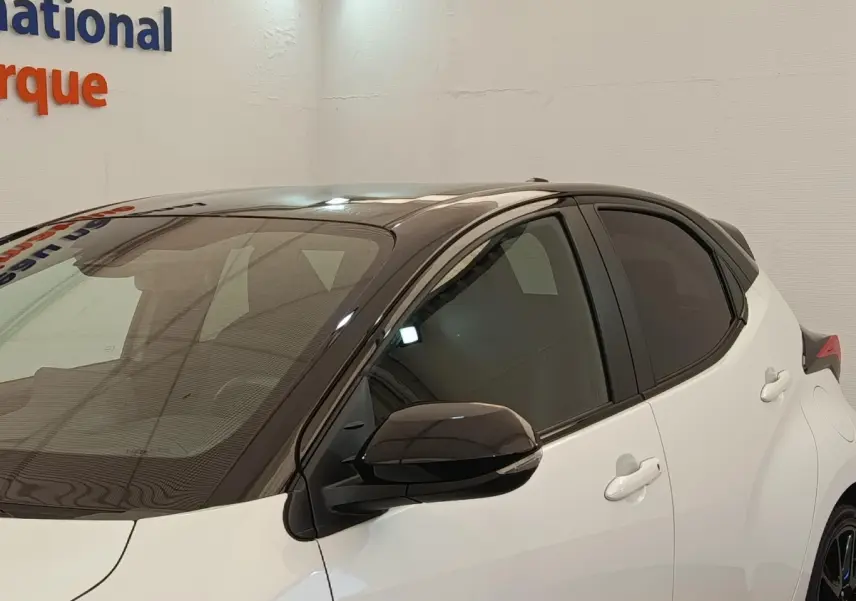 Vue de profil avant droit d'une Toyota Yaris Hybride 116h Collection blanche avec toit noir et rétroviseur noir.