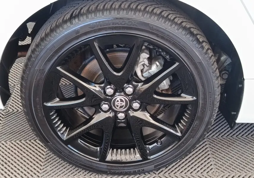 Gros plan sur la roue avant droite noire brillante d'une Toyota Yaris hybride blanche, avec logo Toyota au centre.