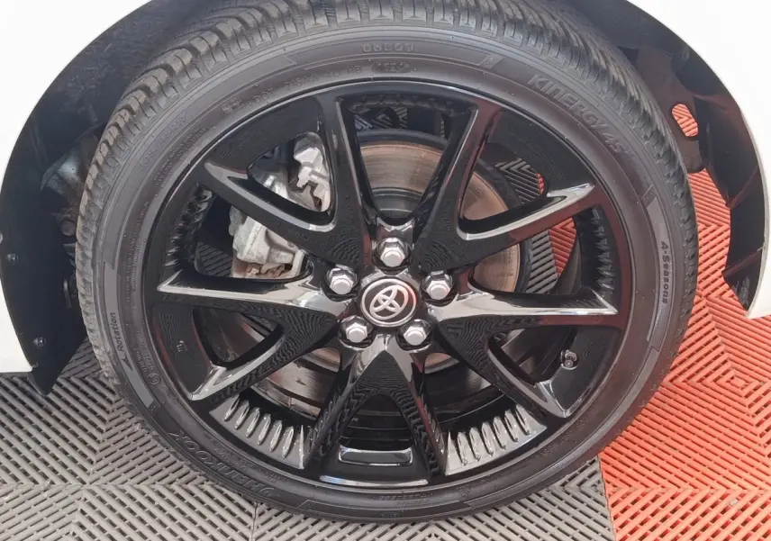 Gros plan sur la roue avant droite noire brillante d'une Toyota Yaris blanche hybride, avec logo Toyota au centre.