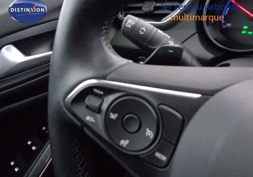 Gros plan sur les commandes au volant noir de l'Opel Grandland X hybride rechargeable, avec tableau de bord partiellement visible.