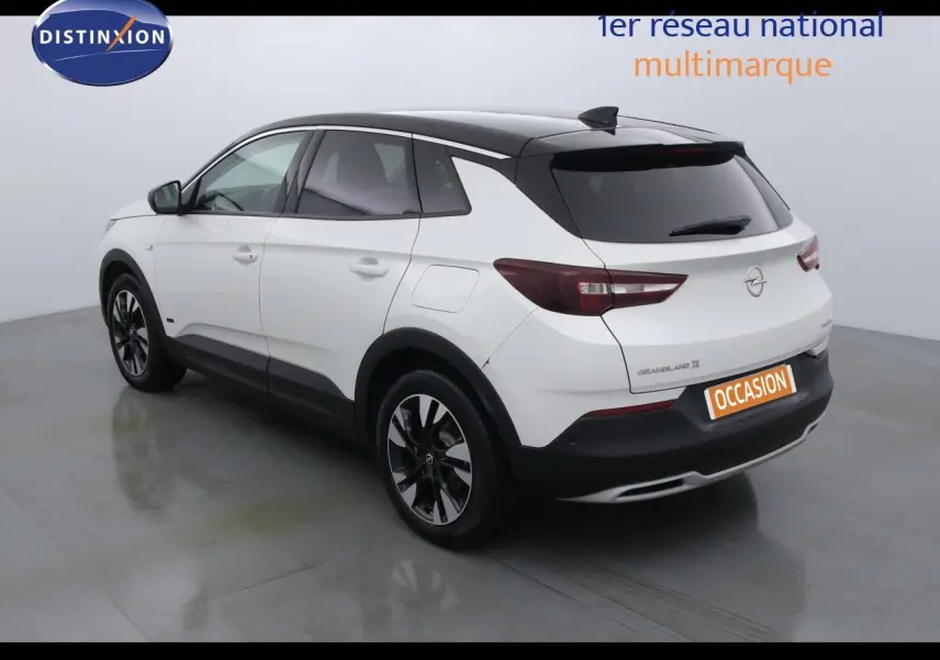 Opel Grandland X hybride blanc perle métal vu en 3/4 arrière côté gauche avec toit noir et jantes bicolores.