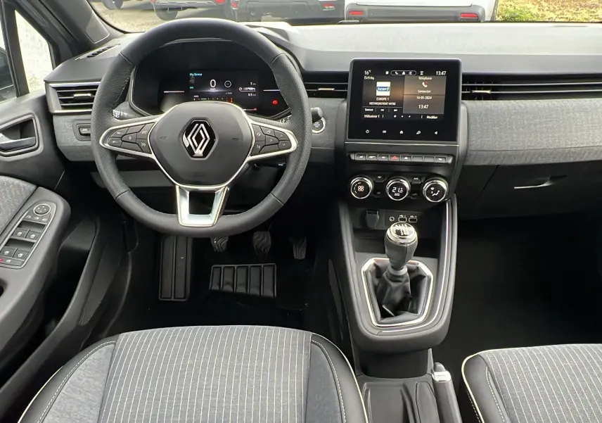 Intérieur de la Renault Clio V TCE 90 TECHNO 2025, vue du poste de conduite avec volant, tableau de bord digital et levier de vitesse manuel.