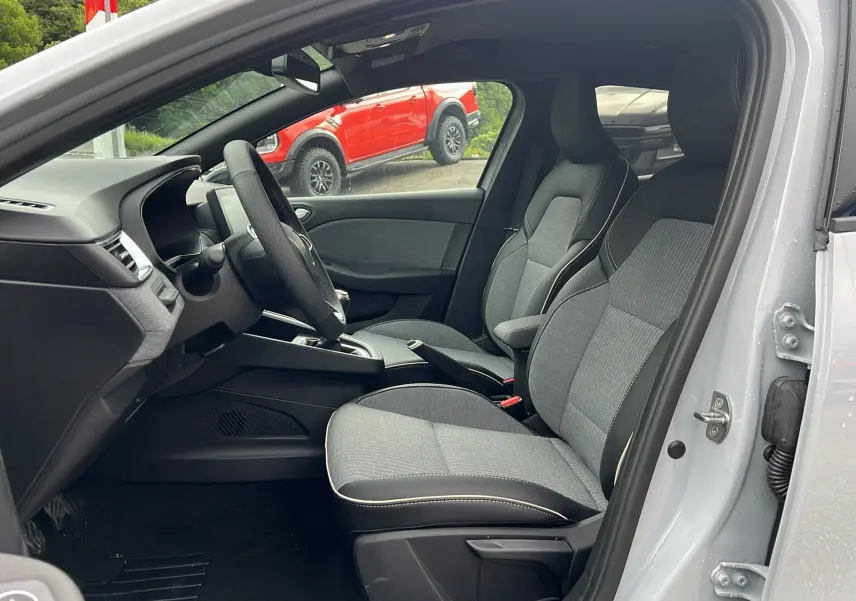 Vue intérieure côté conducteur de la Renault Clio V TCE 90 TECHNO 2025 gris rafale avec sièges tissu bicolore et volant multifonction.