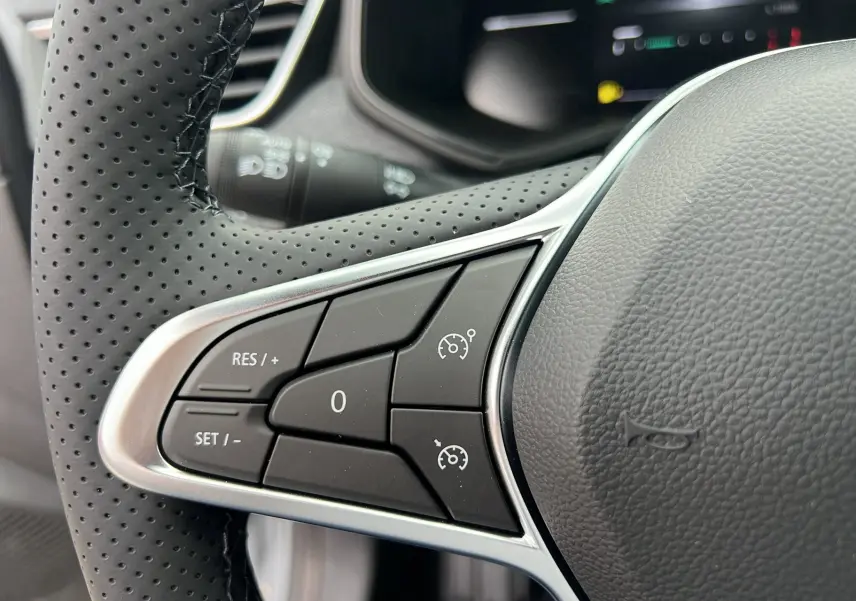 Gros plan sur les commandes de régulateur de vitesse au volant en cuir perforé d'une Renault Clio V TCe 90 Techno gris rafale.