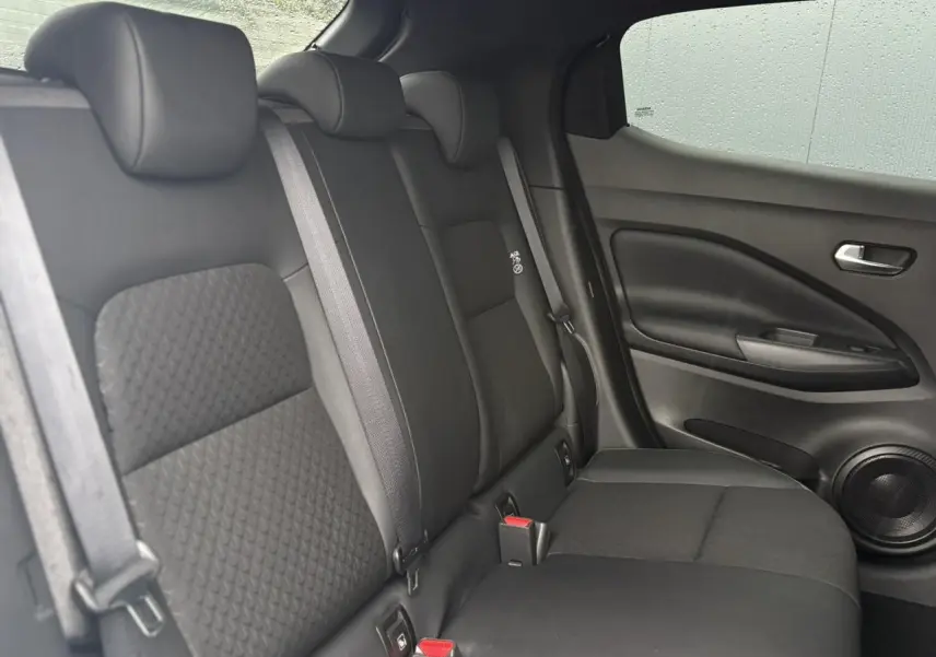 Vue latérale droite de la banquette arrière noire du Nissan Juke 2025 avec ceintures et haut-parleur intégré à la porte