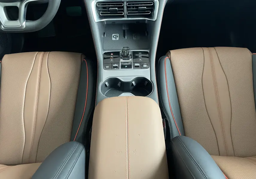 Vue intérieure centrée sur la console centrale et les sièges avant en similicuir vegan marron et noir avec surpiqûres rouges.