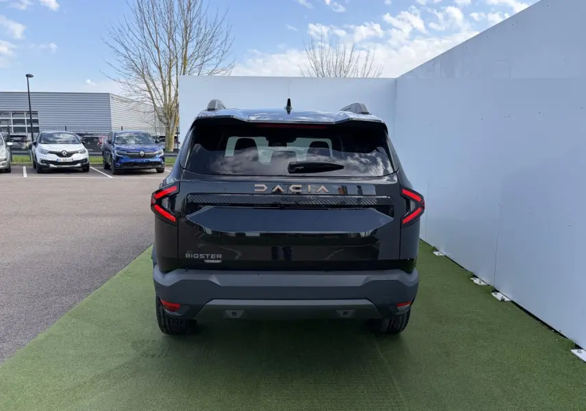 Vue arrière d'un Dacia Bigster noir nacré avec feux LED en forme de C et logo Dacia brun cuivré visible.