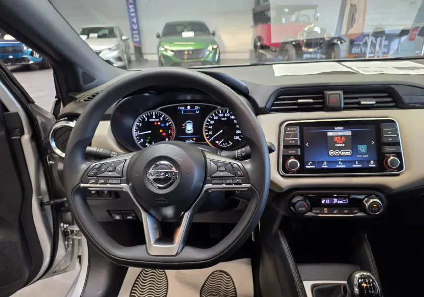 Vue intérieure avant centrée sur le volant Nissan Micra gris clair avec tableau de bord beige et écran tactile 7 pouces.