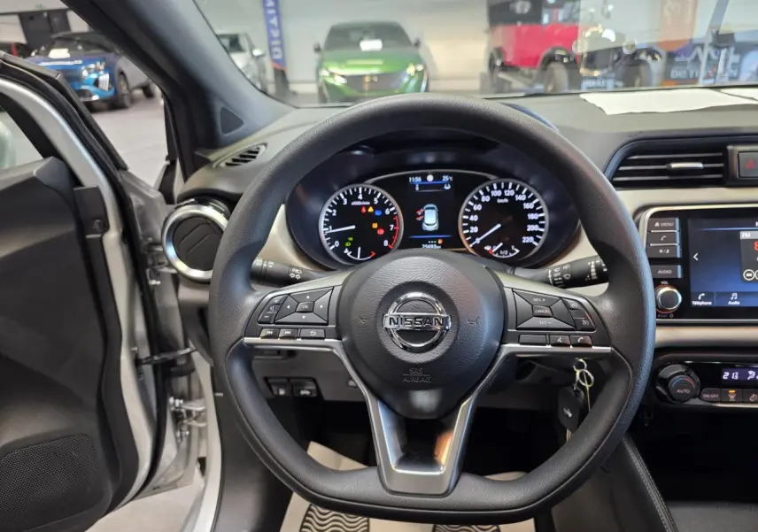 Vue intérieure centrée sur le volant noir de la Nissan Micra gris clair avec tableau de bord et écran tactile visible.