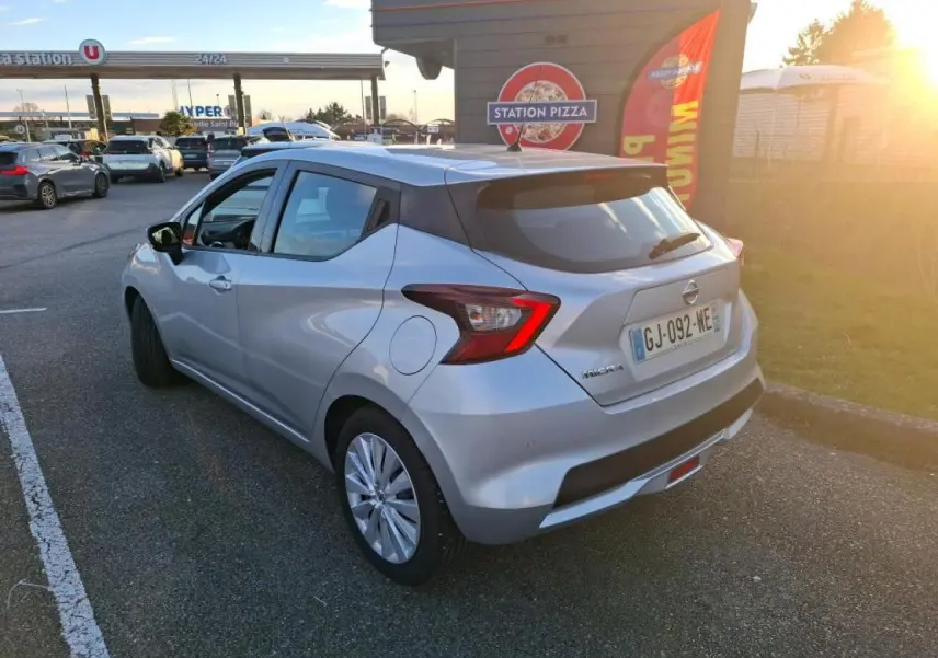 Vue 3/4 arrière droite d'une Nissan Micra gris clair garée près d'une station-service au coucher du soleil.