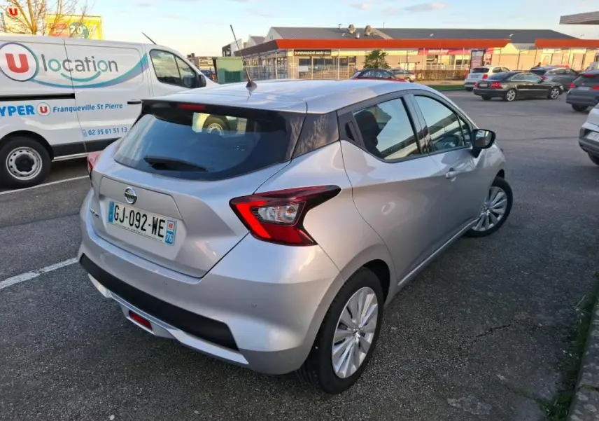 Vue 3/4 arrière droite d'une Nissan Micra gris clair avec jantes en acier et spoiler arrière, stationnée en extérieur.