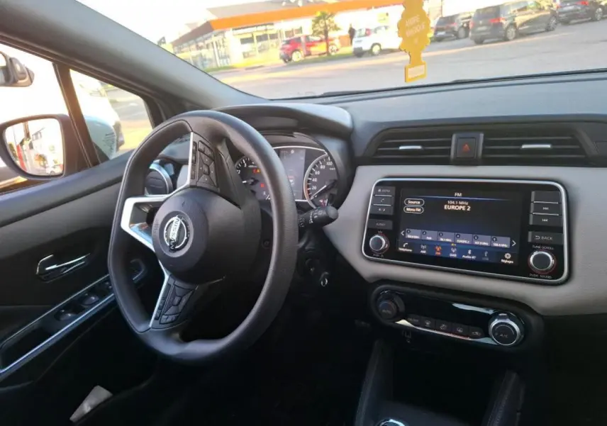 Vue intérieure côté conducteur de la Nissan Micra 2022, tableau de bord beige avec écran tactile et volant multifonction noir.