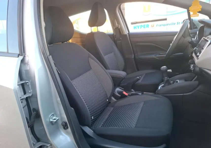 Vue intérieure côté gauche de la Nissan Micra gris clair 2022, montrant les sièges avant en tissu noir et la console centrale.