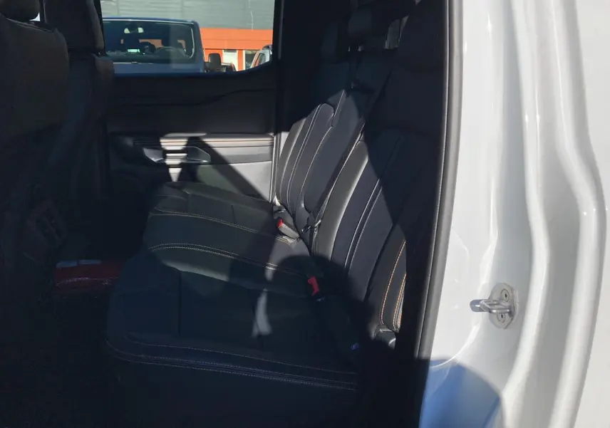 Vue latérale du siège arrière en cuir noir avec surpiqûres orange du Ford Ranger blanc glacier 2026, porte ouverte côté droit.
