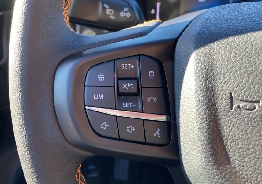 Gros plan sur les commandes multifonctions noires du volant cuir du Ford Ranger Wildtrak blanc glacier.