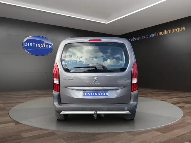 Vue arrière d'un Peugeot Rifter gris foncé 2020 avec attelage et grandes vitres arrière, en showroom multimarque.