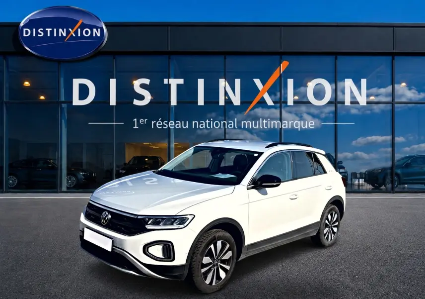 Volkswagen T-Roc blanc en 3/4 avant droit, avec jantes alliage et barres de toit noires visibles.