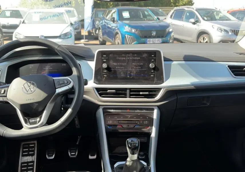 Vue intérieure avant du Volkswagen T-Roc blanc, avec tableau de bord moderne et volant multifonction noir.