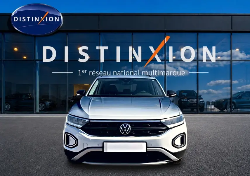 Volkswagen T-Roc blanc vu de face, avec calandre noire et phares LED devant un showroom Distinxion.