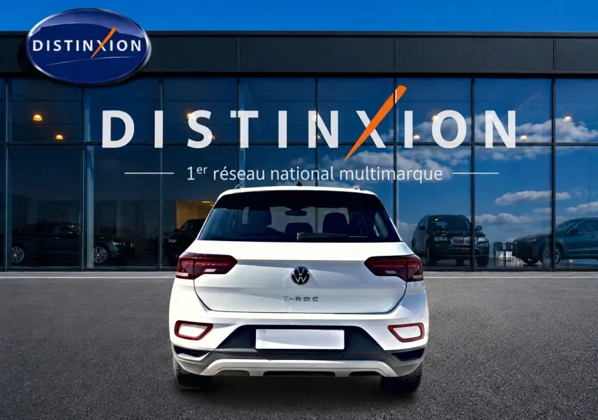 Vue arrière d'un Volkswagen T-Roc blanc 2025 garé devant une vitrine avec logo Distinxion.