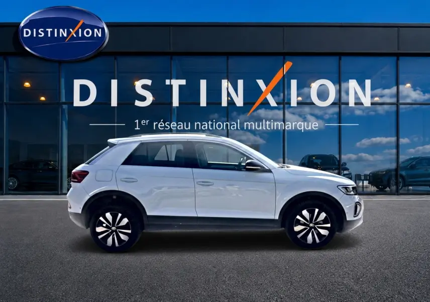 Volkswagen T-Roc blanc en profil droit devant une vitrine avec logo Distinxion visible en arrière-plan.