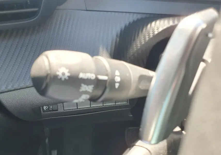 Gros plan sur la commande des feux et clignotants dans l'habitacle d'une Peugeot 208 gris Artense, côté gauche du volant.
