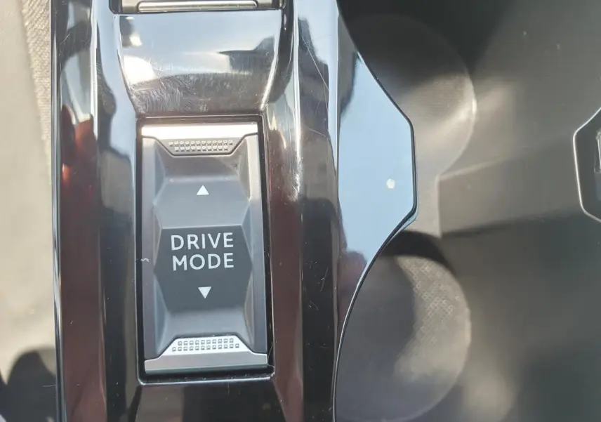Gros plan sur le bouton Drive Mode au centre de la console noire brillante d'une Peugeot 208 gris Artense 2025.
