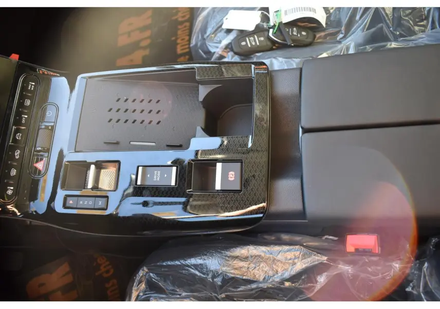 Vue plongeante sur la console centrale noire brillante du Citroën C5 Aircross hybride 2026 avec commandes et porte-clés visibles.
