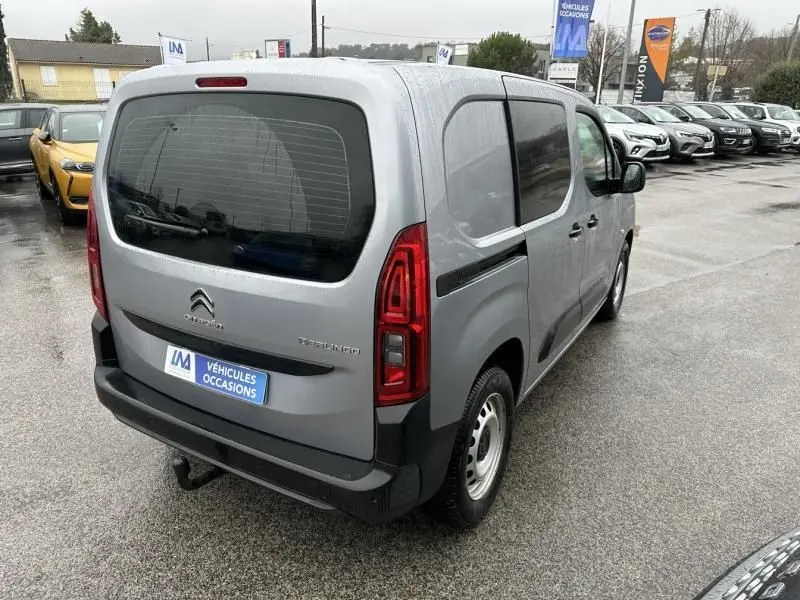 Vue 3/4 arrière droite d'un Citroën Berlingo van gris métal 2020 avec vitres arrière teintées et hayon vitré.