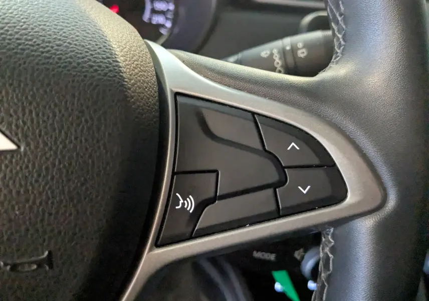 Gros plan sur les commandes vocales et de navigation au volant en cuir noir du Dacia Duster gris 2023.