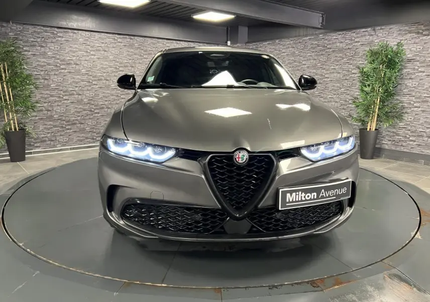 Vue frontale d'une Alfa Romeo Tonale gris foncé avec phares LED allumés et calandre en V distinctive.