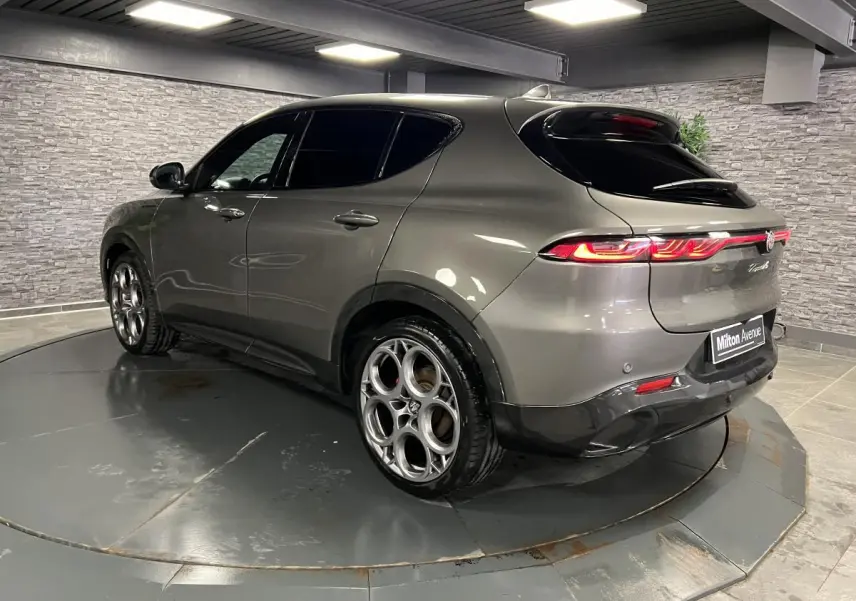 Alfa Romeo Tonale gris foncé vue 3/4 arrière côté gauche, feux arrière allumés et jantes alliage distinctives.